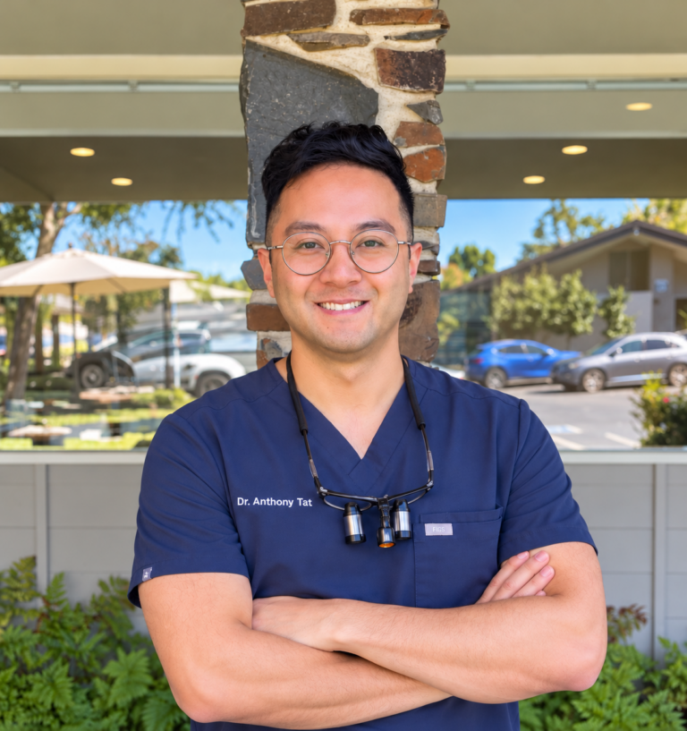 A professional headshot of Dr. Anthony Tat, DDS, smiling in a clean, modern clinic setting at Smile Center Silicon Valley.